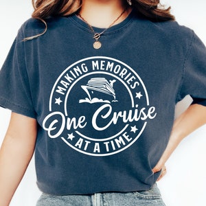 Pode incluir: Uma camiseta azul marinho com um gráfico circular branco que diz "Making Memories One Cruise At A Time" com um navio de cruzeiro branco dentro do círculo.