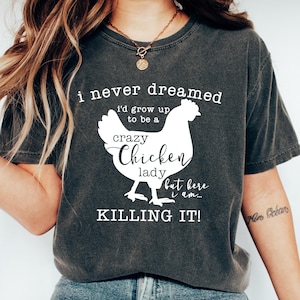 May include: A grey t-shirt with a white graphic of a chicken and the text "i never dreamed i'd grow up to be a crazy Chicken lady but here i am... KILLING IT!"