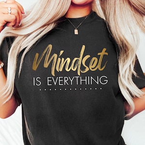 Può includere: Una maglietta nera con lettering in oro che recita "Mindset is Everything".