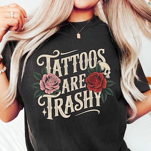 May include: Black t-shirt with the text "Tattoos Are Trashy" in a vintage style font. The text is surrounded by roses and a skull.