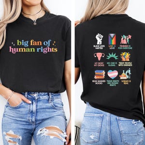 May include: Black t-shirt with the text "big fan of human rights" in colorful letters on the front. The back of the shirt features various graphics and phrases, including "Black Lives Matter" and "Trans Rights are Human Rights."