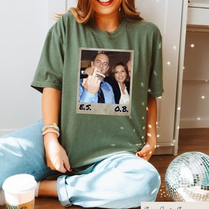 May include: A green t-shirt with a photo of two people. The photo is in a white frame with the text "E.S." and "O.B." written below it.
