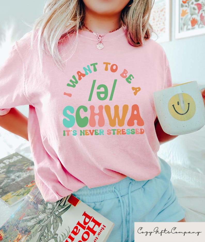 May include: Pink t-shirt with a colorful graphic that says "I want to be a /e/ SCHWA It's never stressed".
