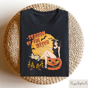 May include: Black t-shirt with a graphic of a witch sitting on a pumpkin. The graphic says "Season of the Witch".