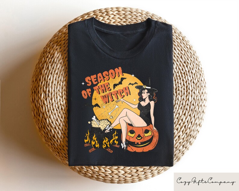 May include: Black t-shirt with a graphic of a witch sitting on a pumpkin. The graphic says "Season of the Witch".