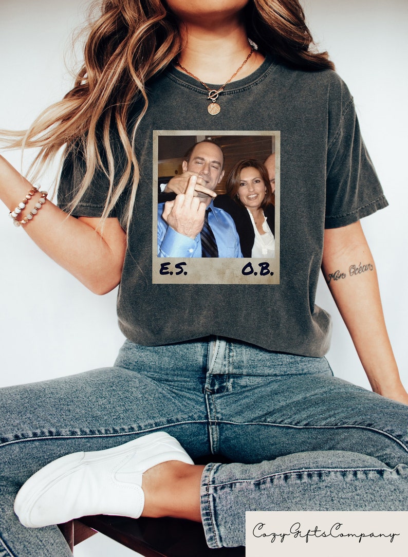 May include: A black t-shirt with a vintage-style photo of two people. The photo is in a white frame with the text "E.S." and "O.B." written below it.