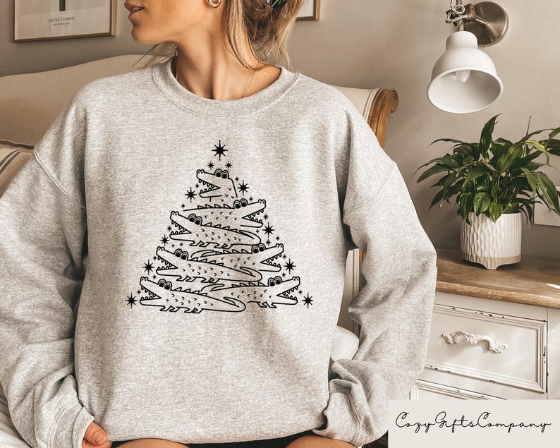 May include: A gray sweatshirt with a black and white graphic of alligators stacked to form a Christmas tree. The graphic includes a star at the top of the tree.