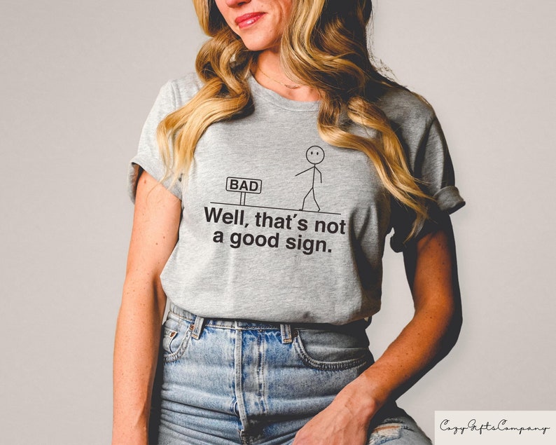 May include: Gray t-shirt with a stick figure walking towards a sign that says "BAD". The text on the shirt reads "Well, that's not a good sign."