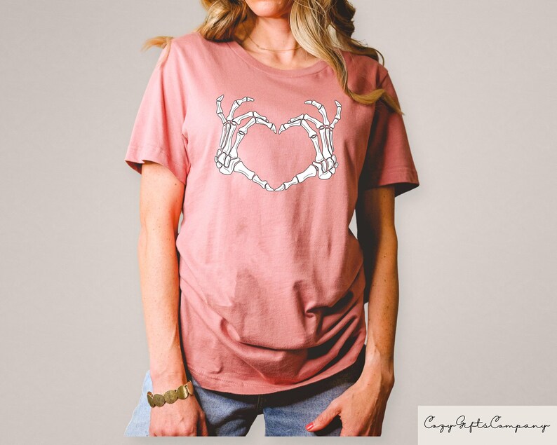 Może przedstawiać: R&oacute;żowy t-shirt z białym nadrukiem szkieletu dłoni tworzącym kształt serca. Nadruk głosi "Love You To Death".