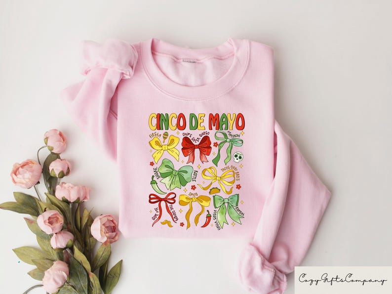 May include: Pink sweatshirt with a graphic design of colorful bows and the text "Cinco de Mayo".