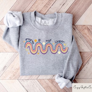 May include: Gray sweatshirt with a rainbow design and the text "Progress is not linear".