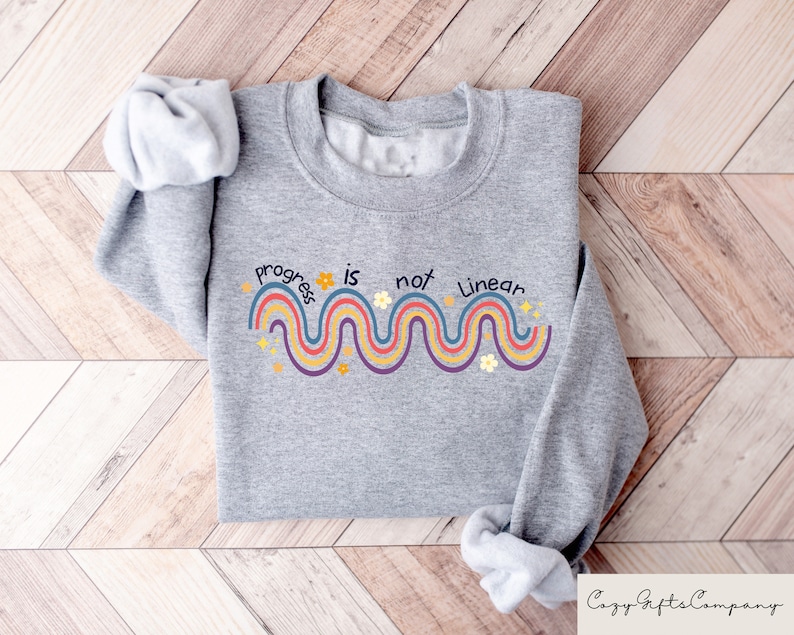 May include: Gray sweatshirt with a rainbow design and the text "Progress is not linear".