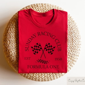 Puede incluir: Camiseta roja con un gr&aacute;fico negro que dice "Sunday Racing Club Est. 1950 Formula One" con un dise&ntilde;o de bandera a cuadros.