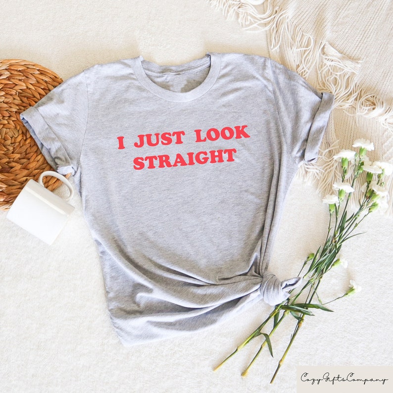 May include: Gray t-shirt with the text "I JUST LOOK STRAIGHT" in red.