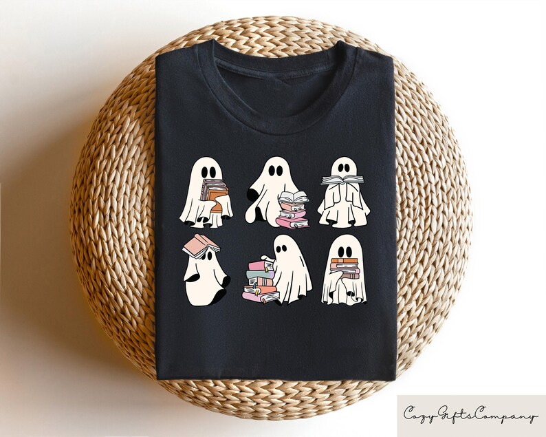 Puede incluir: Camiseta negra con un gr&aacute;fico de seis fantasmas sosteniendo pilas de libros. Los fantasmas son blancos con ojos y bocas negros. Los libros son rosas, azules y blancos.