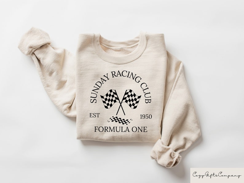 Puede incluir: Una sudadera beige con un dise&ntilde;o gr&aacute;fico negro que dice "Sunday Racing Club Est 1950 Formula One" con un dise&ntilde;o de bandera a cuadros.