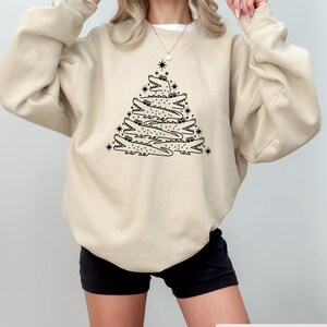 May include: A beige sweatshirt with a black alligator Christmas tree design. The tree is made up of alligators stacked on top of each other, with their eyes and mouths open. The tree is topped with a star.