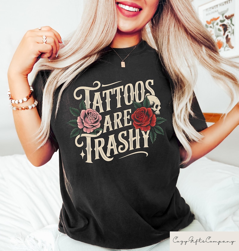 May include: Black t-shirt with the text "Tattoos Are Trashy" in a vintage style font. The text is surrounded by roses and a skull.