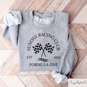 Puede incluir: Sudadera gris con un dise&ntilde;o gr&aacute;fico negro que dice "Sunday Racing Club Est 1950 Formula One" con un dise&ntilde;o de bandera a cuadros.