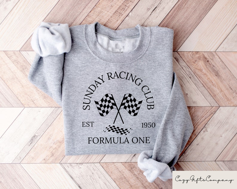 Puede incluir: Sudadera gris con un dise&ntilde;o gr&aacute;fico negro que dice "Sunday Racing Club Est 1950 Formula One" con un dise&ntilde;o de bandera a cuadros.