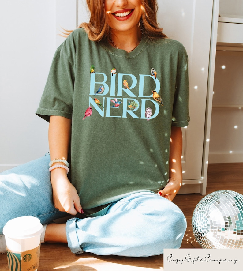 May include: A green t-shirt with the text "BIRD NERD" in blue letters. The shirt is decorated with a variety of colorful birds.