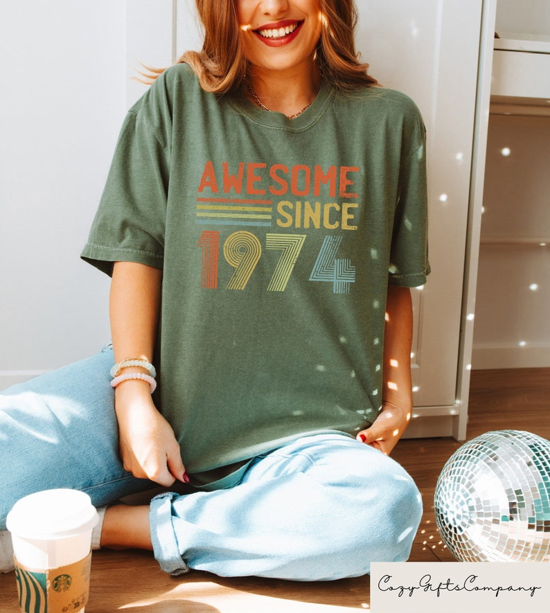 Pu&ograve; includere: Una maglietta verde con il testo "Awesome Since 1974" in un design retr&ograve; arcobaleno.