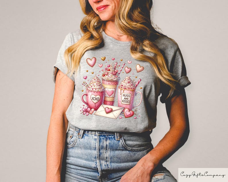 May include: A gray t-shirt featuring a watercolor design of three coffee drinks with whipped cream, hearts, and the phrases "XOXO" and "Hugs and Kisses." A heart-shaped envelope and flowers are also included in the design.