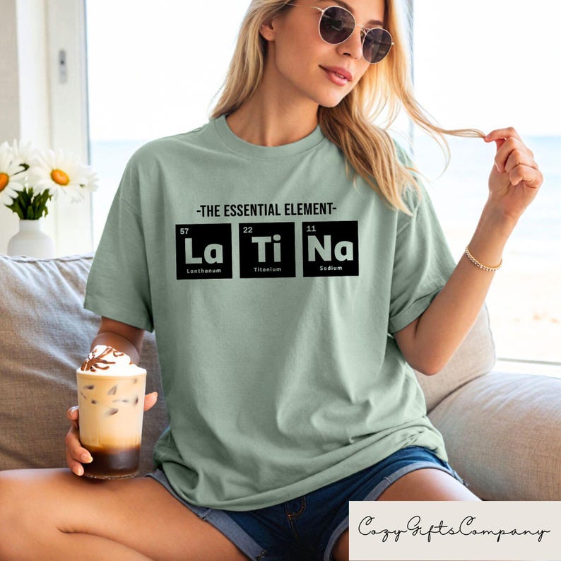 May include: A light green t-shirt with a graphic of the periodic table elements La, Ti, and Na. The text "The Essential Element" is above the graphic.