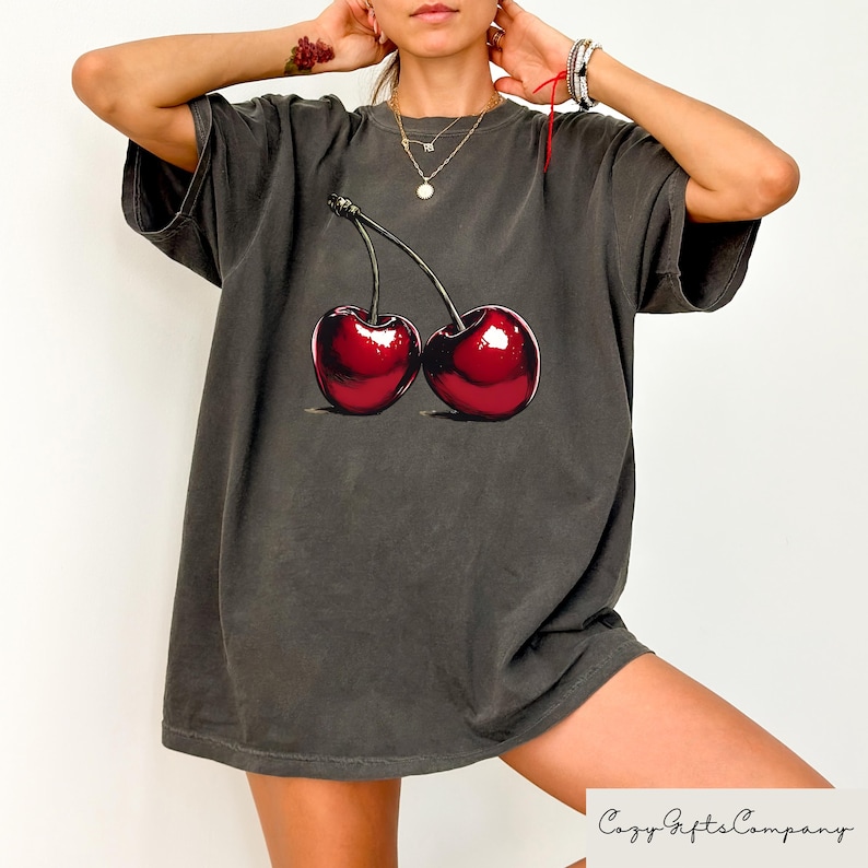 May include: A dark gray oversized t-shirt with a graphic of two red cherries on the front.