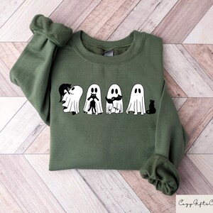 May include: A green sweatshirt with a graphic of five ghosts holding black cats. The ghosts are white and have black eyes and mouths. The cats are black and have white eyes.
