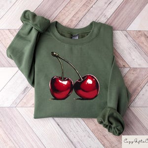 May include: A green sweatshirt with a graphic of two red cherries on the front.