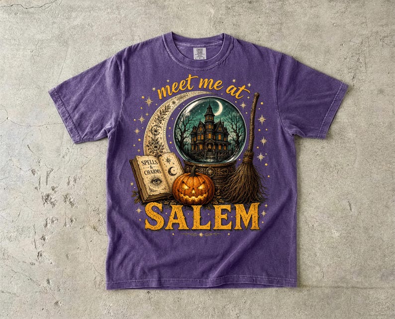 May include: A purple short-sleeve t-shirt featuring a graphic print with the text 'meet me at SALEM'. The design includes a crescent moon, a crystal ball showing a haunted house, an open book labeled 'SPELLS & CHARMS', a jack-o'-lantern, and a broom.