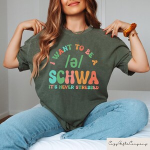 May include: A green t-shirt with the text "I want to be a /ə/ SCHWA It's never stressed" in colorful, retro-style lettering.