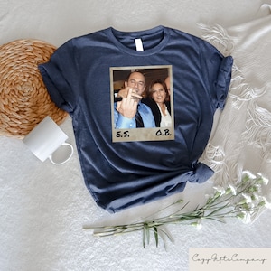 May include: A navy blue t-shirt with a photo of two people. The photo is in a white frame with the text "E.S." and "O.B." underneath.