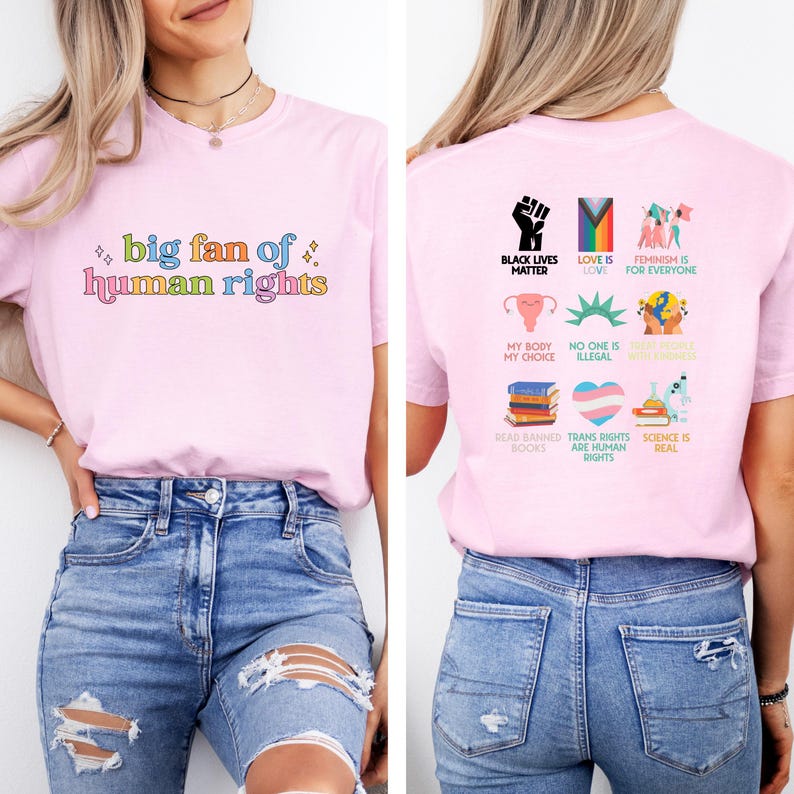 May include: A light pink t-shirt with the text "big fan of human rights" in colorful letters. The back of the shirt features various graphics and phrases, including "Black Lives Matter" and "Love is Love."