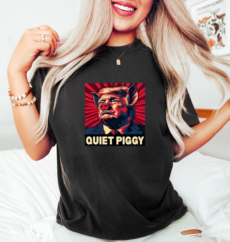 May include: Black t-shirt featuring a graphic of a pig-like face with the text "QUIET PIGGY" in a bold font. The graphic has red, blue, and yellow tones. The shirt is a dark color.