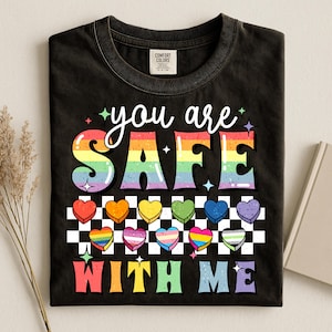 May include: Black t-shirt with the words "you are SAFE WITH ME" in a rainbow design. The shirt features rainbow-coloured hearts and a chequered pattern.