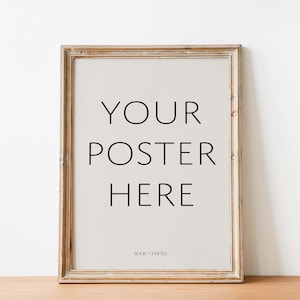 Puede incluir: Un póster enmarcado con el texto "YOUR POSTER HERE" en negro, fuente sans-serif. El marco es de madera marrón claro envejecida. El póster está sobre un fondo beige claro, con el texto "BOOK CHAPTER" en la parte inferior.