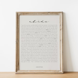 May include: A framed print with a beige background and black text. The text is a passage from the Bible, John 15, about abiding in Christ. The title of the passage is "Abide".