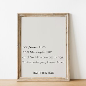 Op de afbeelding: Een ingelijste print met een lichtbeige achtergrond en zwarte tekst. De tekst luidt: "Want uit Hem en door Hem en tot Hem zijn alle dingen. Hem zij de heerlijkheid in eeuwigheid. Amen. Romeinen 11:36". De lijst is lichtbruin.