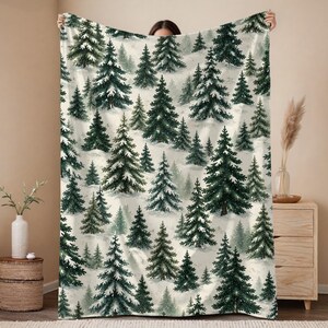 Può includere: Una coperta rettangolare con un motivo ripetuto di alberi di pino verde scuro coperti di neve bianca su uno sfondo chiaro e innevato. Il design raffigura un fitto paesaggio boschivo con conifere di varie dimensioni.