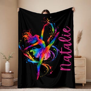 May include: A black throw blanket featuring a vibrant, multi-colored watercolor-style illustration of a ballet dancer in a dynamic pose. The design includes swirling paint splatters in rainbow hues and the name Natalie written in pink script.
