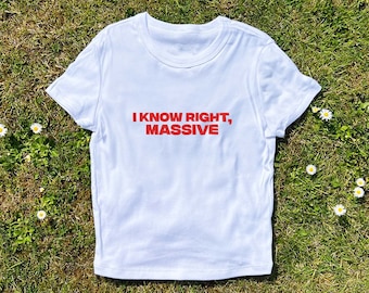 以下が含まれることがあります： 白いTシャツに赤い文字で「I KNOW RIGHT, MASSIVE」と書かれています。Tシャツは緑の芝生と白い花の上に置かれています。