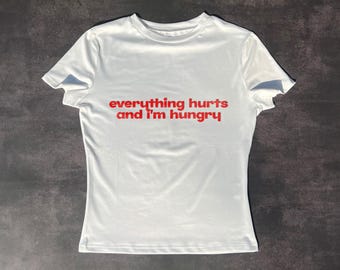 May include: White t-shirt with the text "everything hurts and I'm hungry" printed in red.