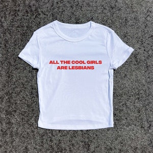 May include: White t-shirt with the red text "ALL THE COOL GIRLS ARE LESBIANS". The shirt has short sleeves and a crew neck. The shirt is made of a soft, comfortable material.