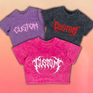 Peut inclure: Trois t-shirts délavés à l'acide, violets, gris anthracite et rose vif. Chaque t-shirt porte le mot "CUSTOM" dans une police gothique stylisée. Les t-shirts sont à manches courtes et coupés, avec un aspect texturé.