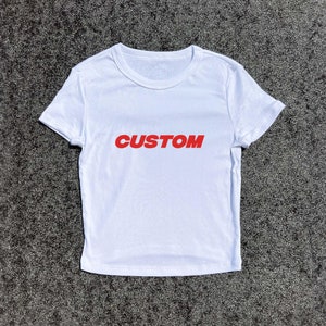 Könnte beinhalten: Weißes, kurzes T-Shirt mit dem Wort "CUSTOM" in Rot auf der Vorderseite.