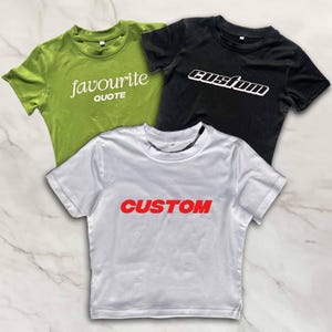 Puede incluir: Tres camisetas recortadas con diferentes dise&ntilde;os. Una es verde con el texto "favourite quote", otra es negra con el texto "custom" en blanco, y otra es blanca con el texto "CUSTOM" en rojo.