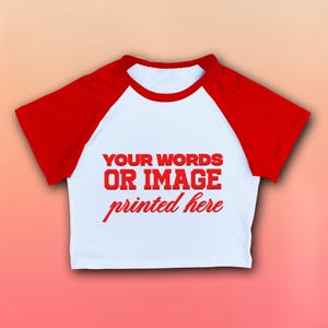 May include: White crop top with red raglan sleeves. The shirt features the text "YOUR WORDS OR IMAGE printed here" in red. The top has a round neckline and is made of a soft material.
