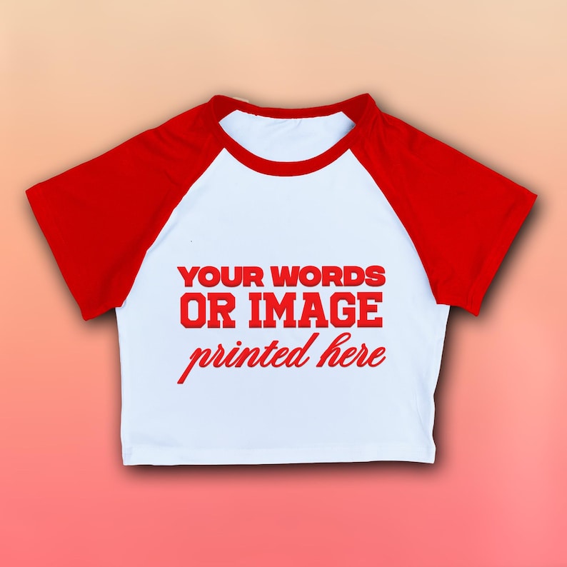May include: White crop top with red raglan sleeves. The shirt features the text "YOUR WORDS OR IMAGE printed here" in red. The top has a round neckline and is made of a soft material.